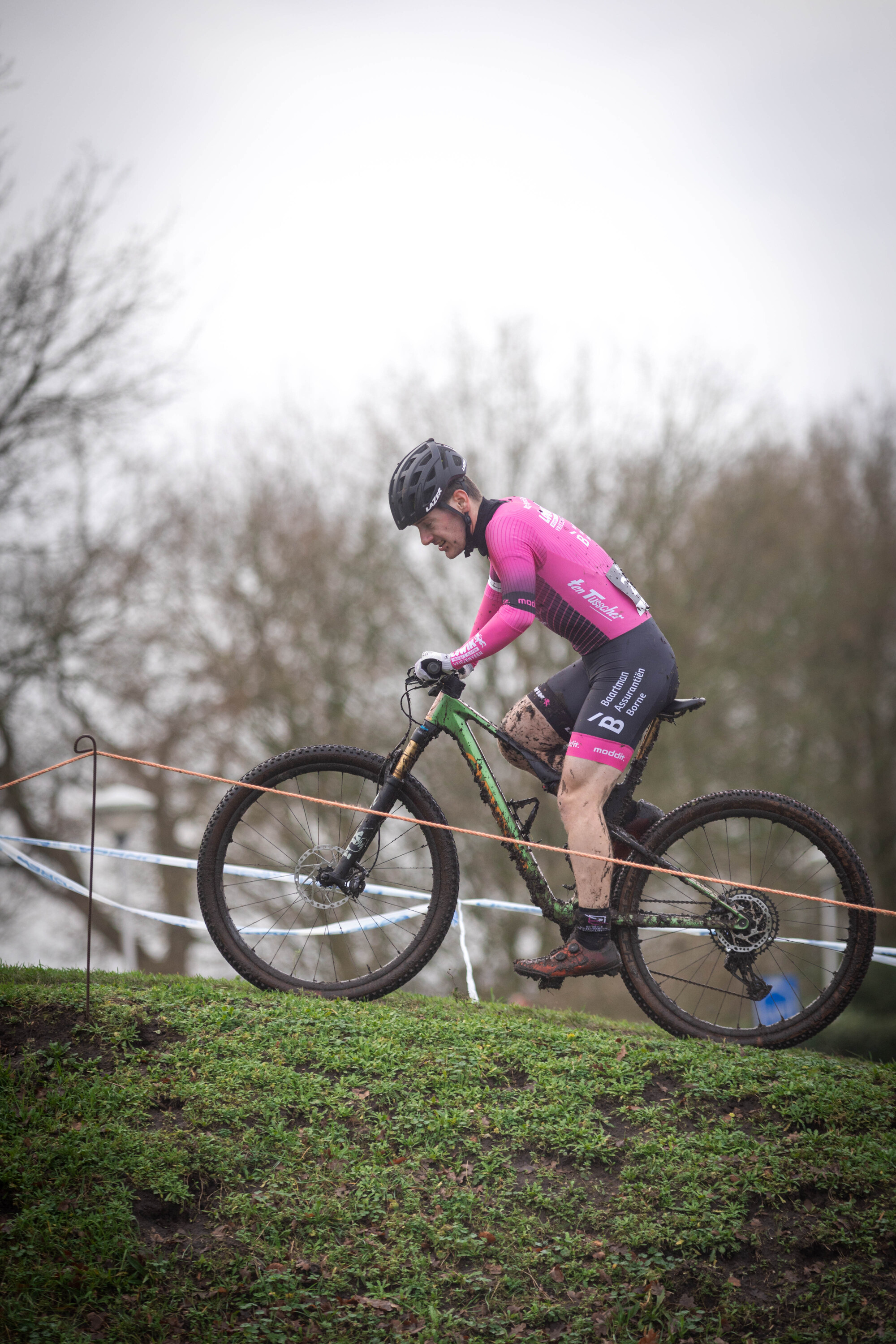 A man in a black and pink jersey is riding his bicycle over the top of a hill.