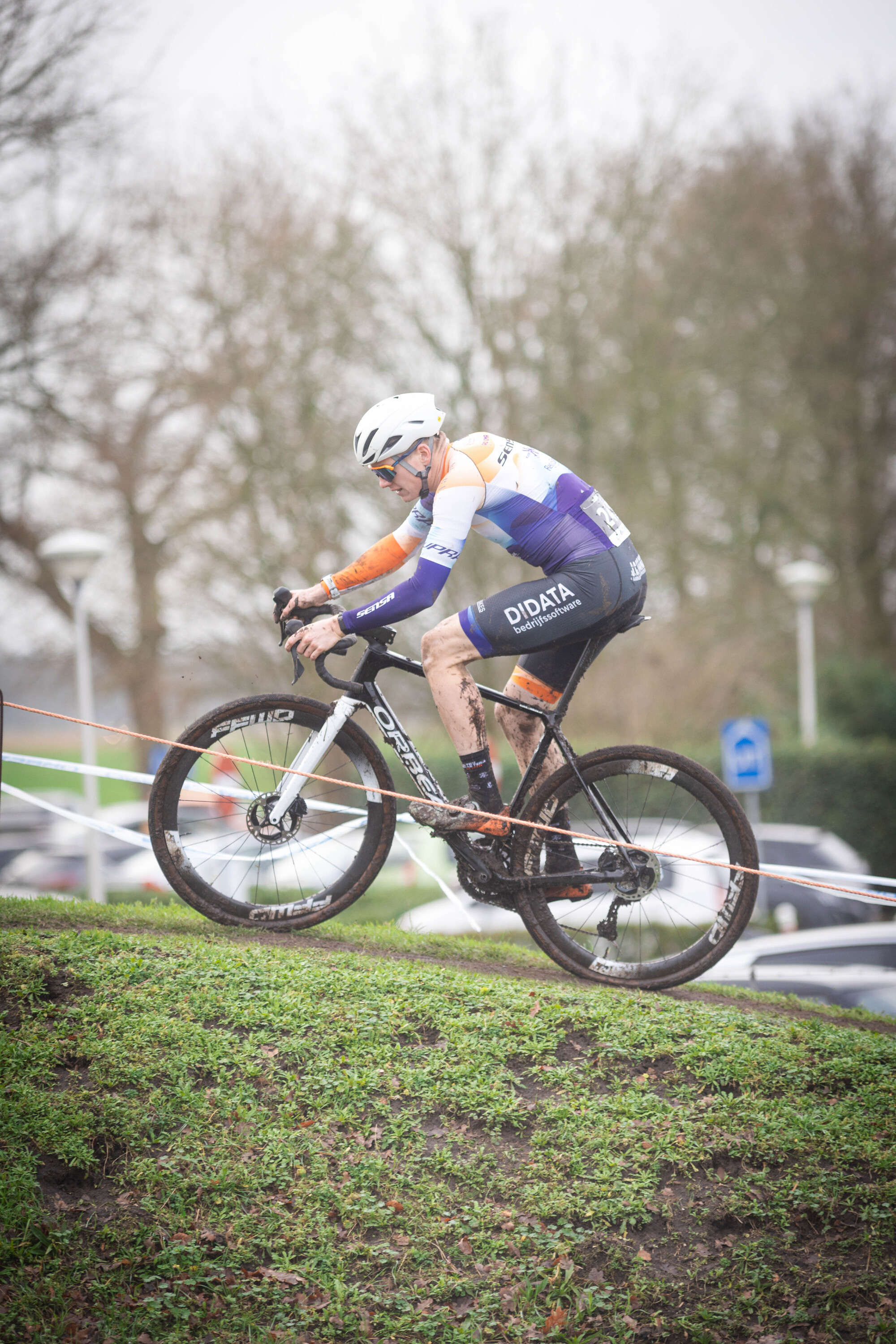 A cyclist wearing a white helmet and jersey riding his bike on grass.