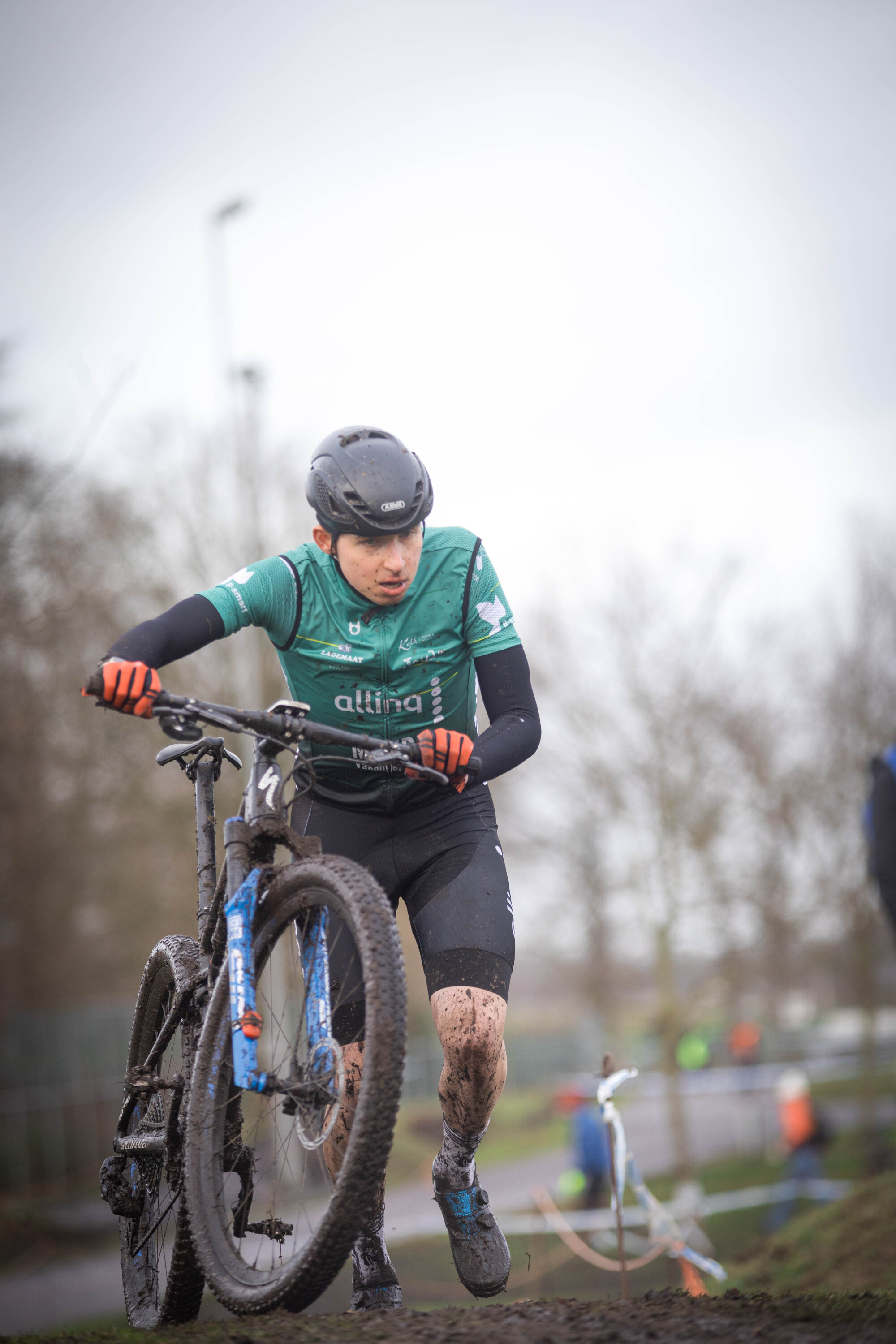 A person riding a blue and white mountain bike wearing a green GOW Raalte shirt.