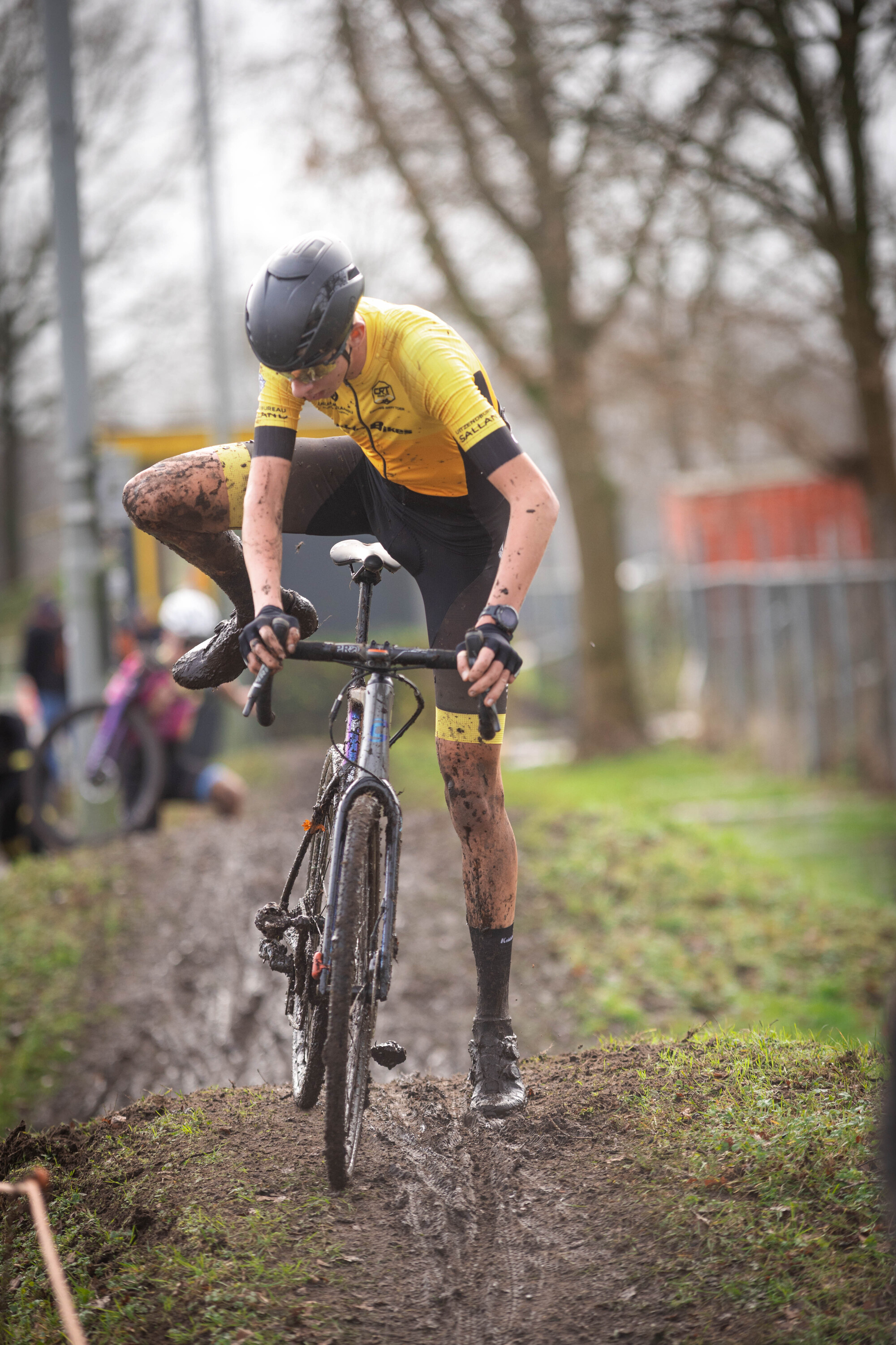 A man in a yellow shirt riding his bike through muddy terrain.