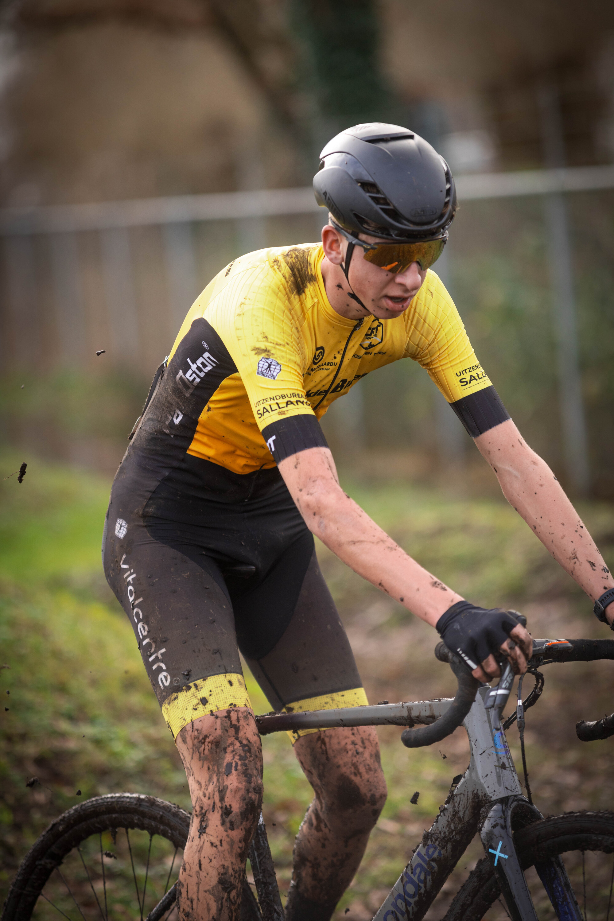 A man in black and yellow riding a bicycle covered in mud.