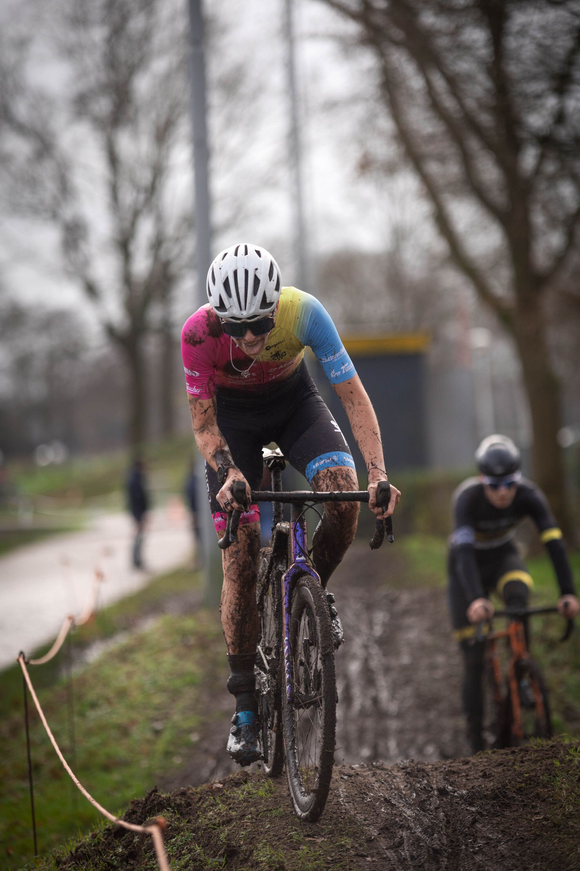 Two people riding bicycles on a trail with one wearing a pink and yellow jersey.