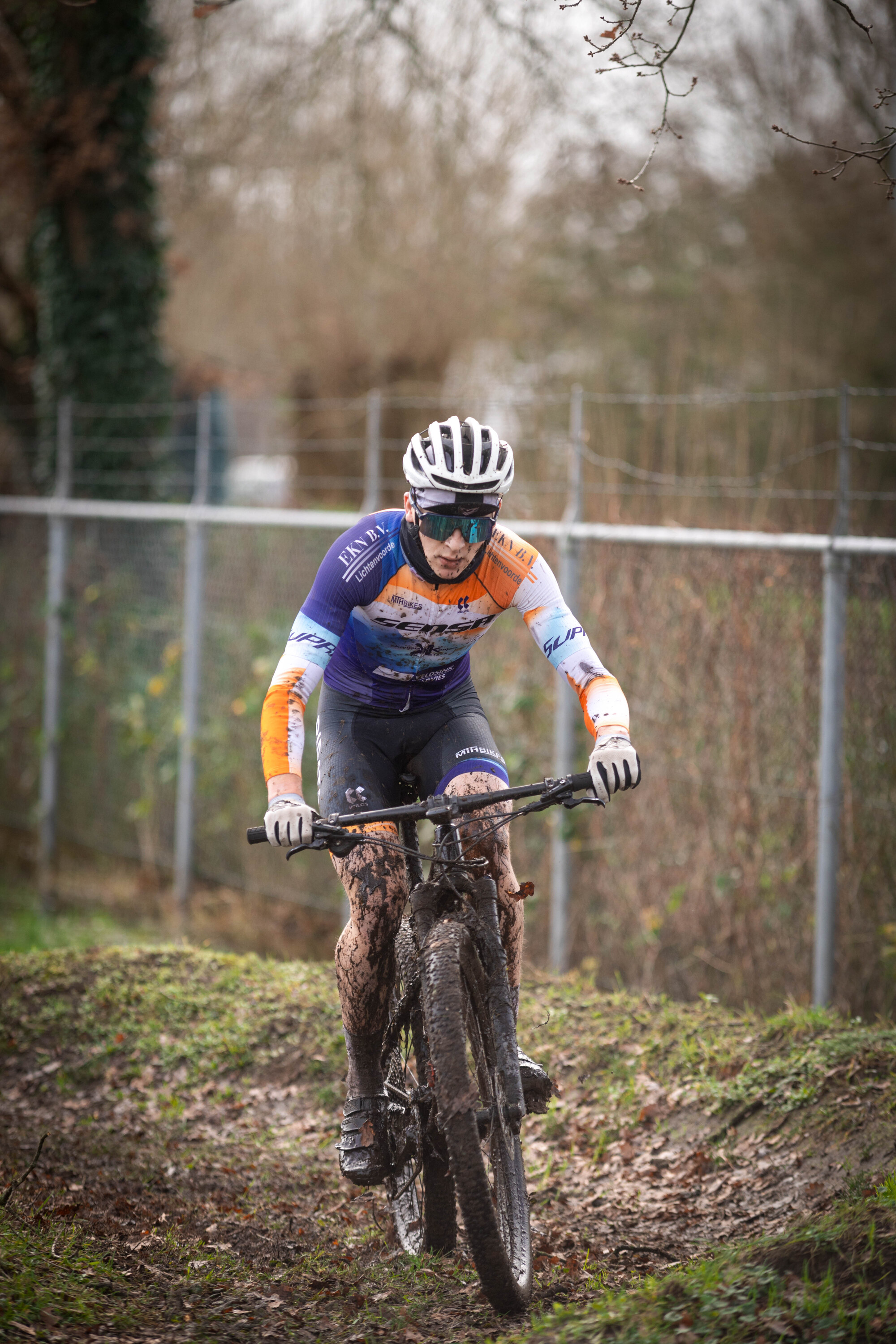 A woman wearing an orange and blue shirt is riding a bike.