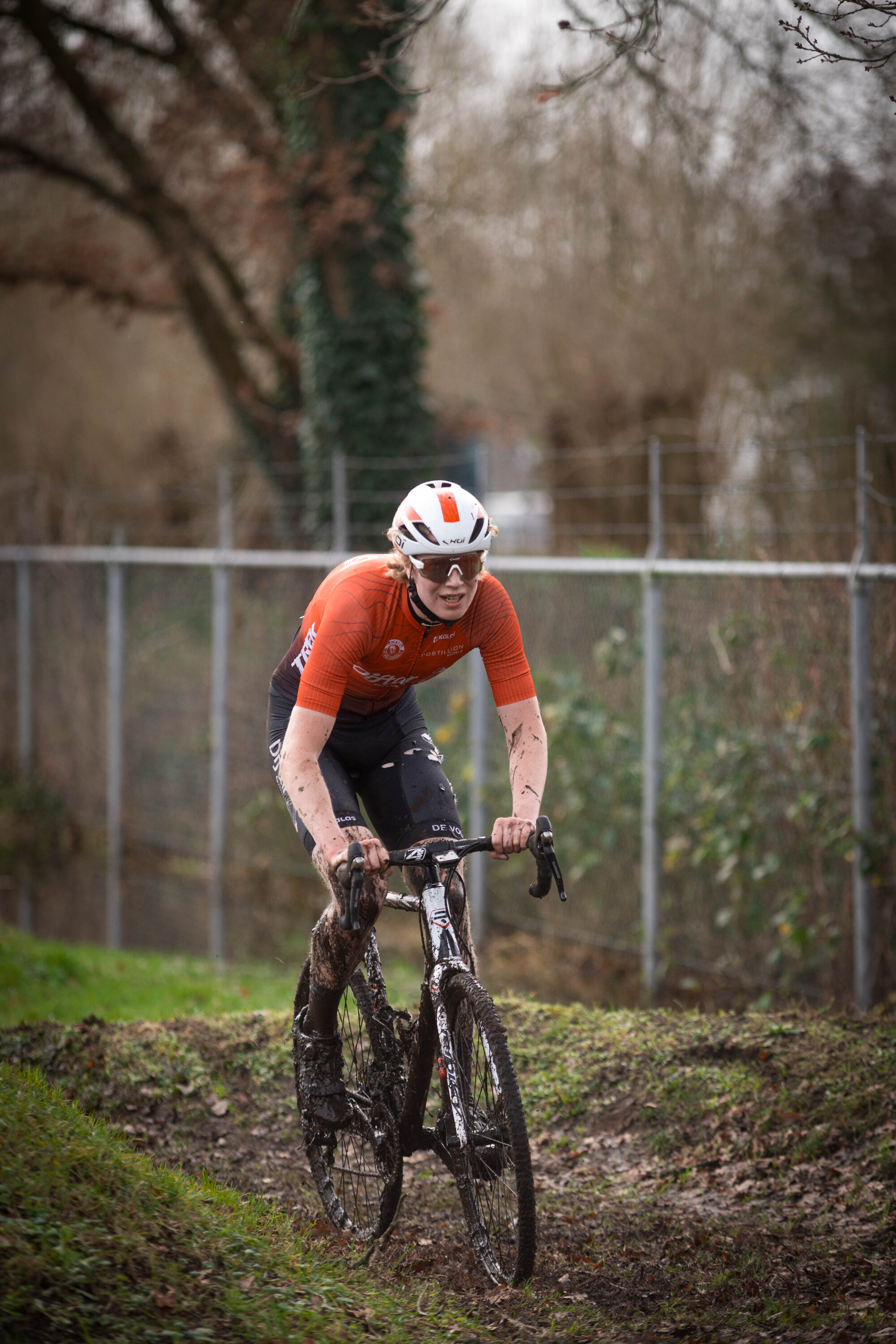 A man in a red jersey is riding a dirty bike on a muddy path.