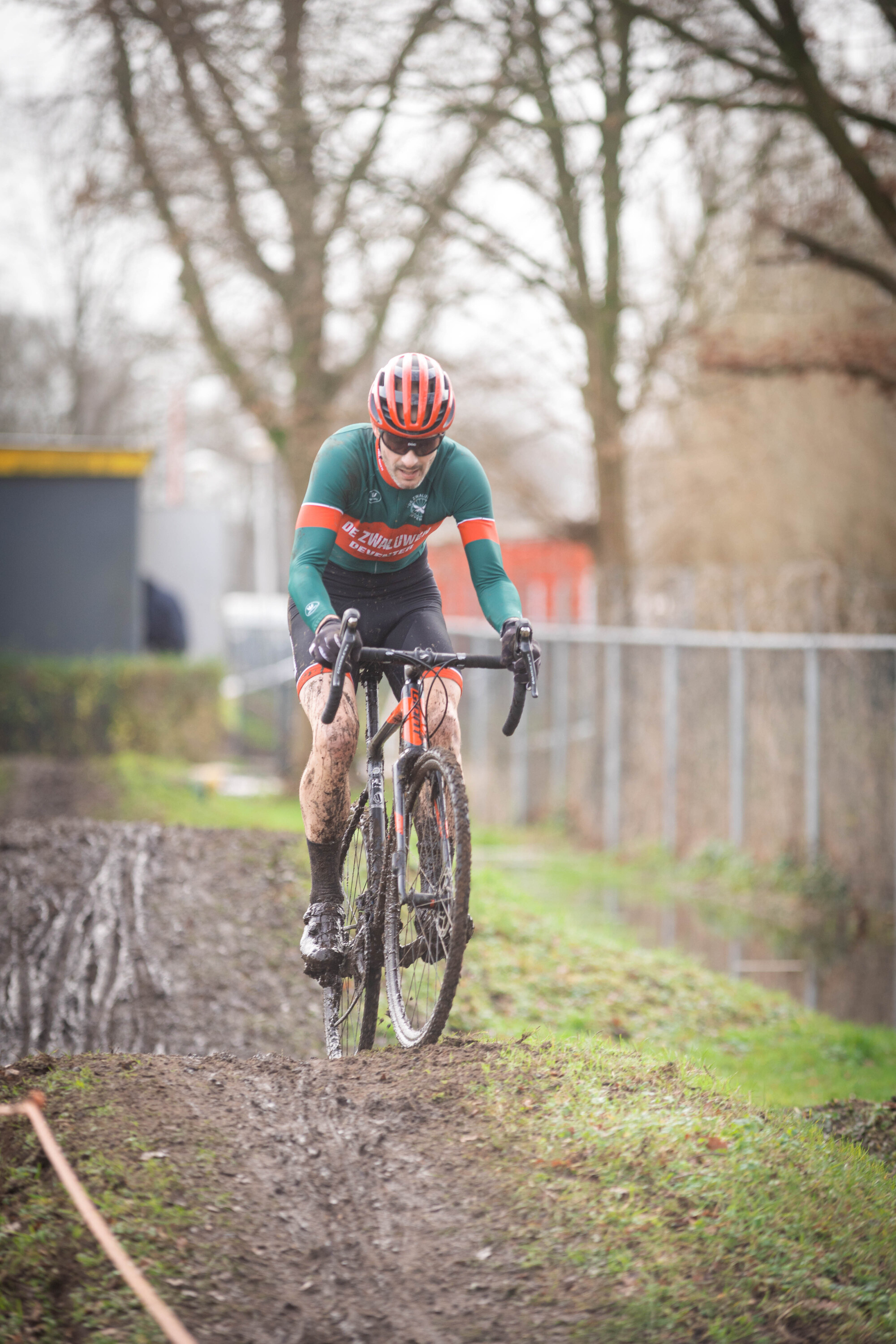 A man in a green and red shirt rides a bike down a muddy hill.