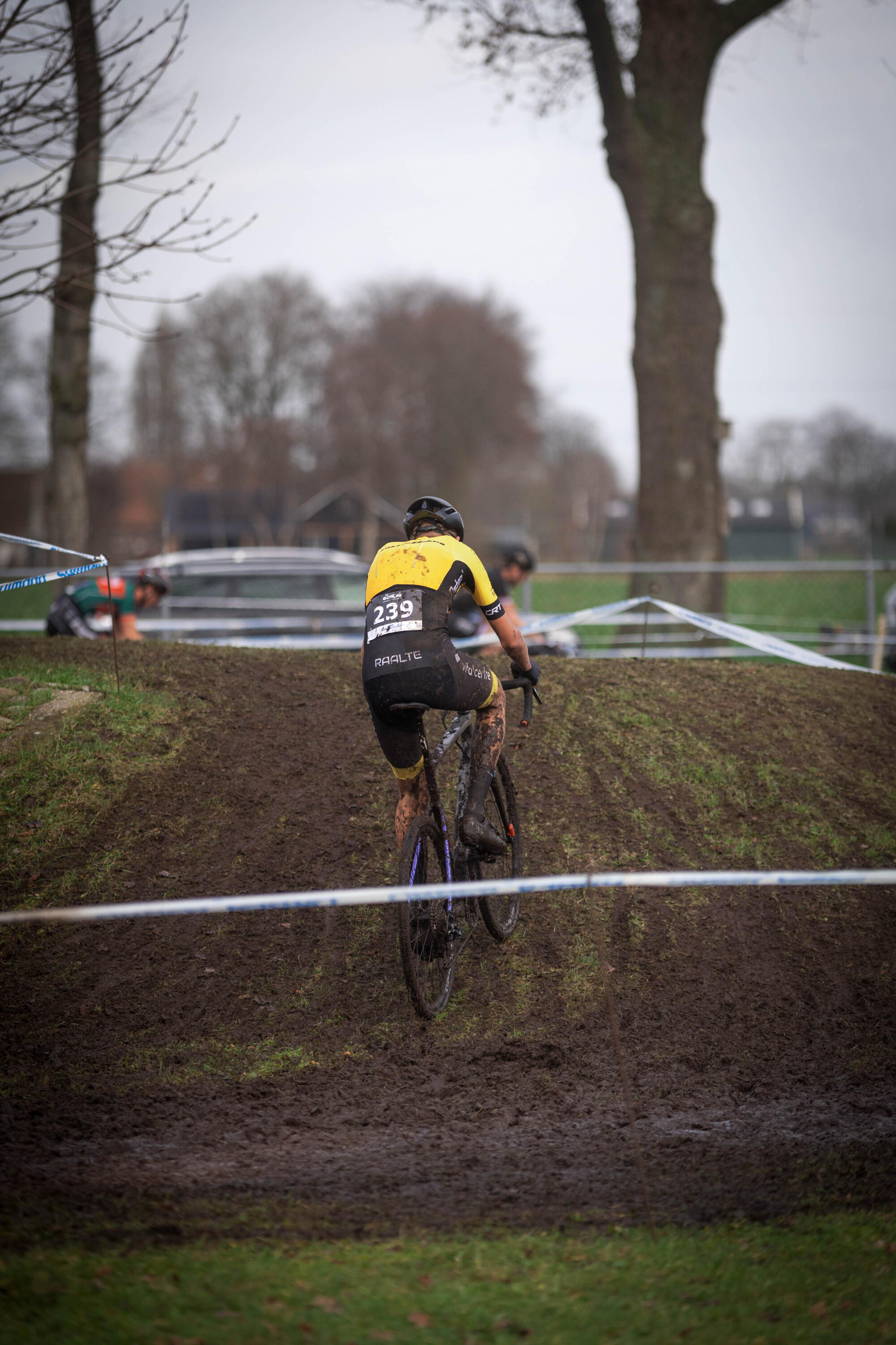 A man in a black and yellow bicycle uniform is riding his bike on a muddy track.