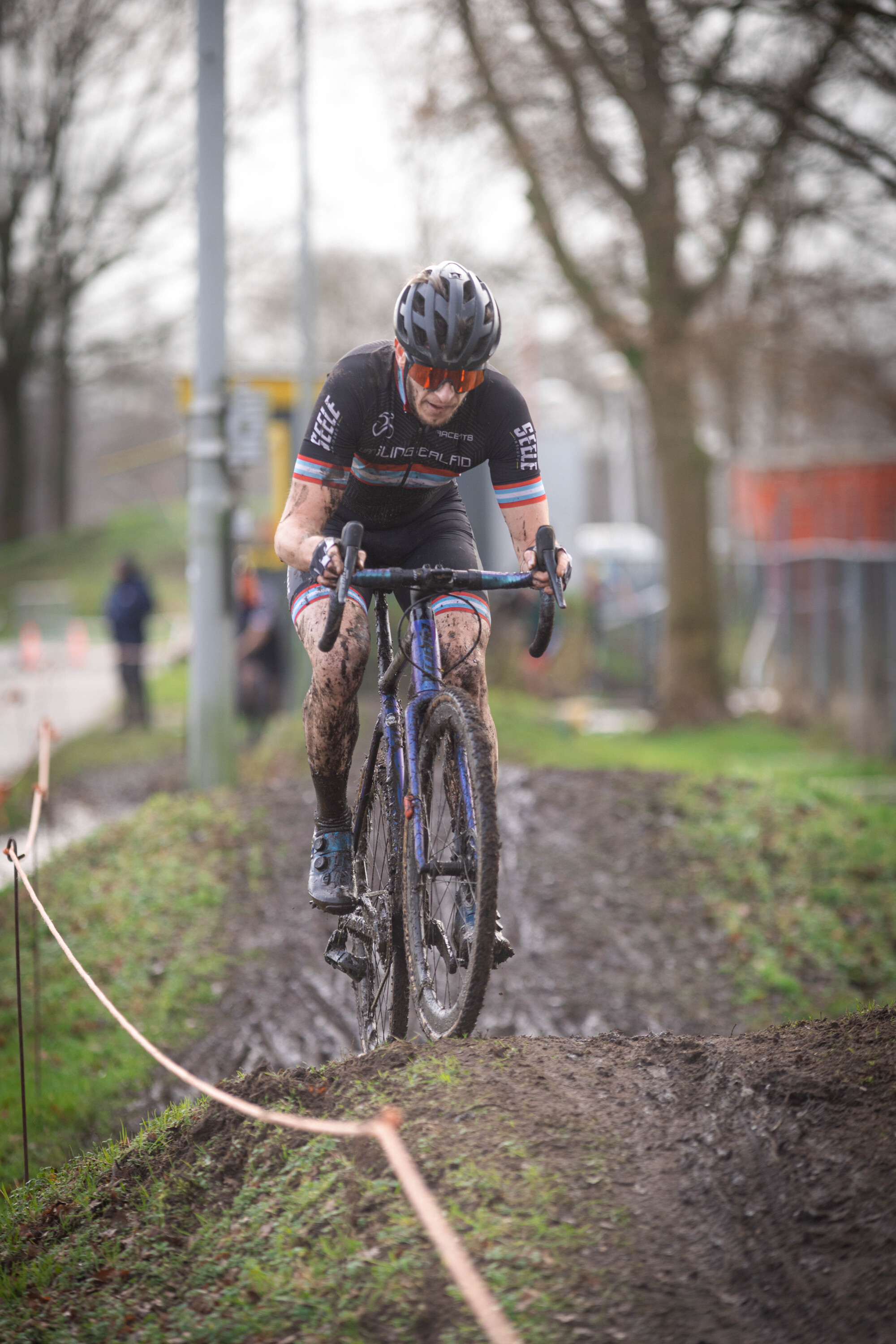 A man is riding a bike on muddy ground. He has a number 23 on his jersey and a red and white logo on his helmet.