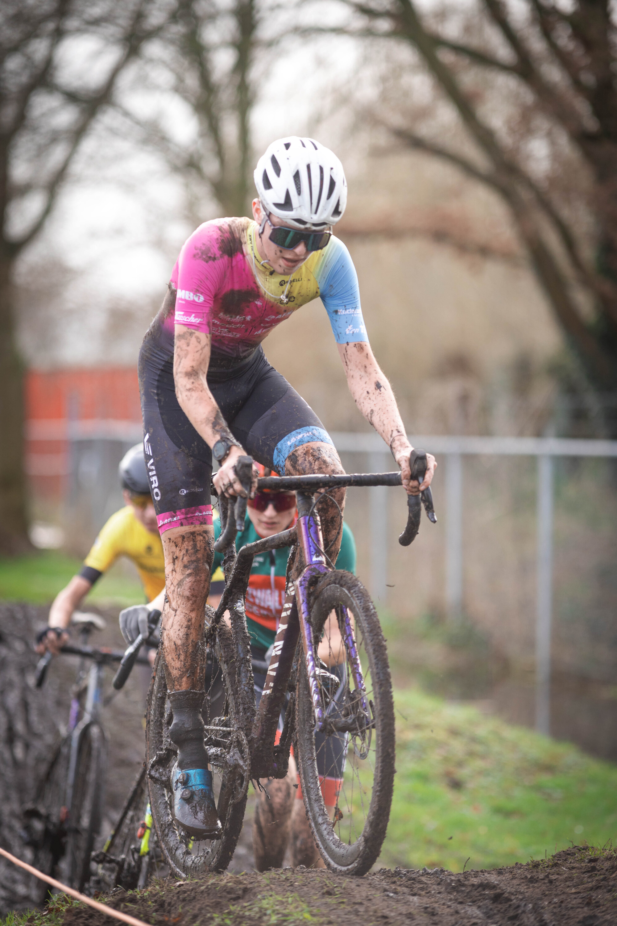 A woman wearing pink and blue bike racing gear is riding her bicycle on a course.