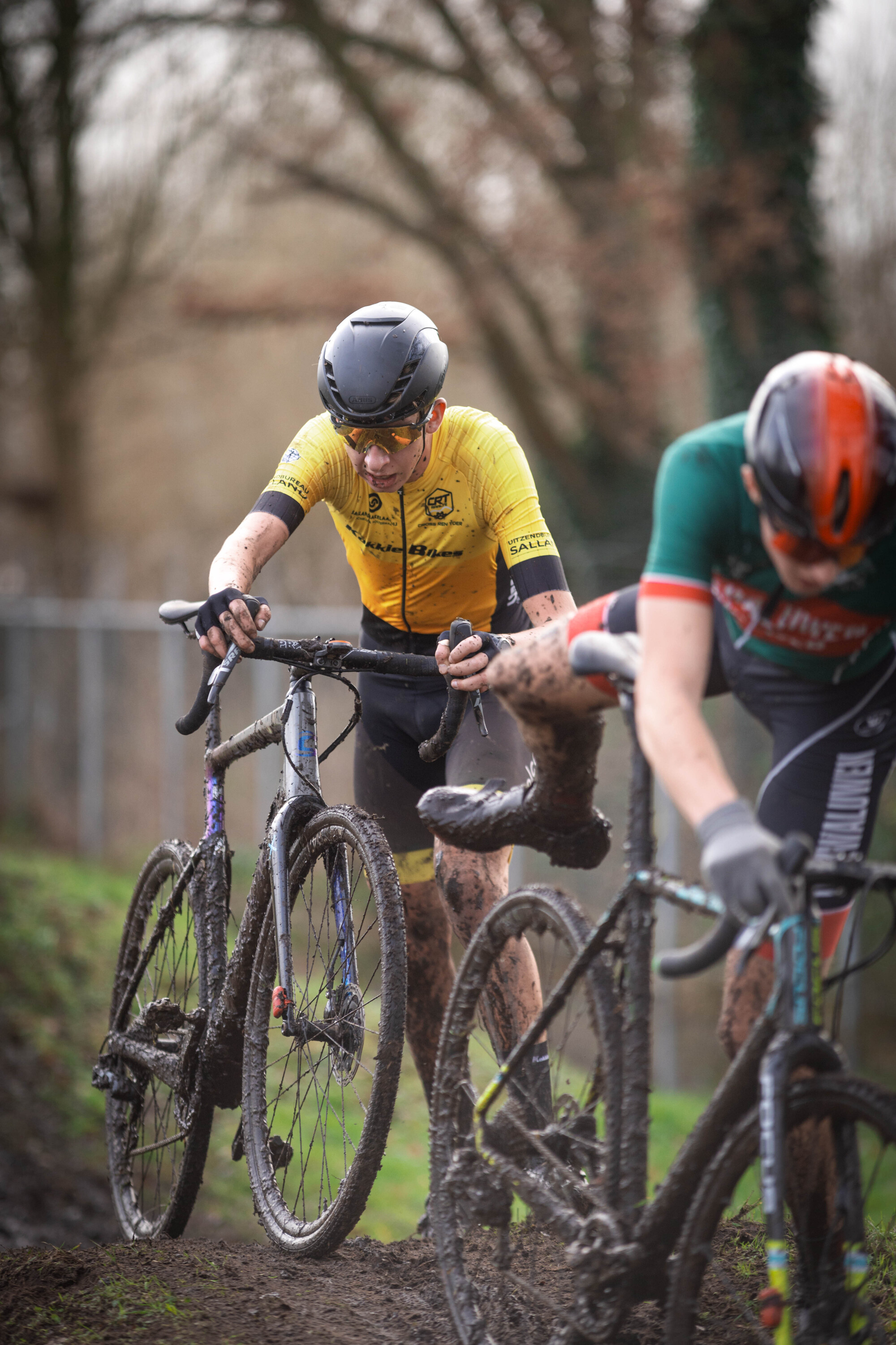 Two men race on a muddy track with bikes in a cyclocross race.