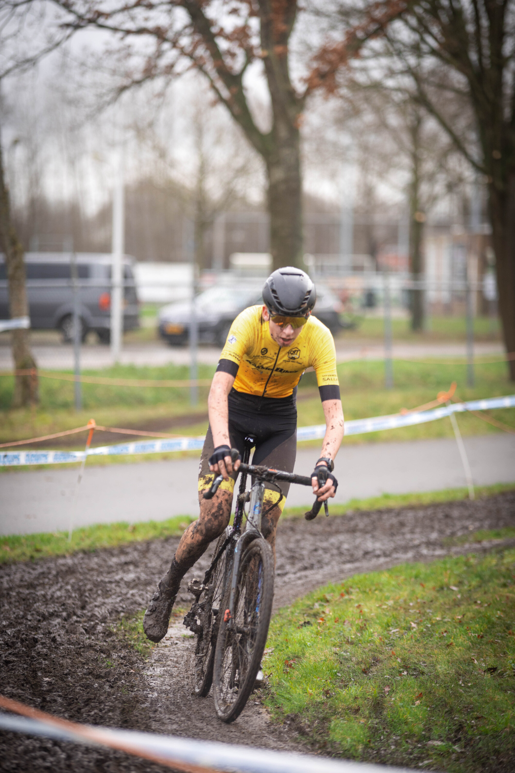 A cyclist with the number 2 on his black and yellow jersey races down a muddy path.