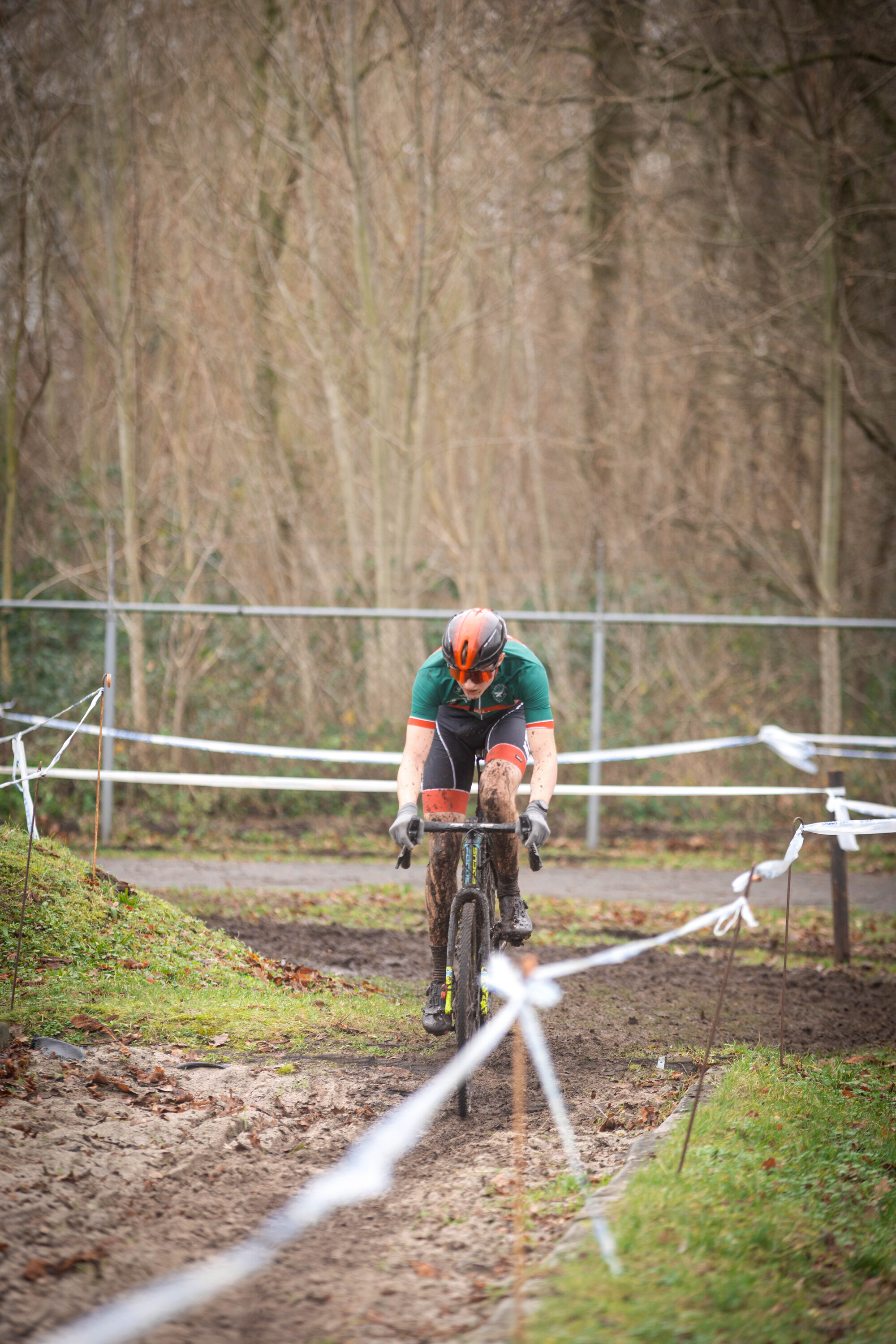 A man in a green shirt riding a bike on a dirt track behind a white rope.