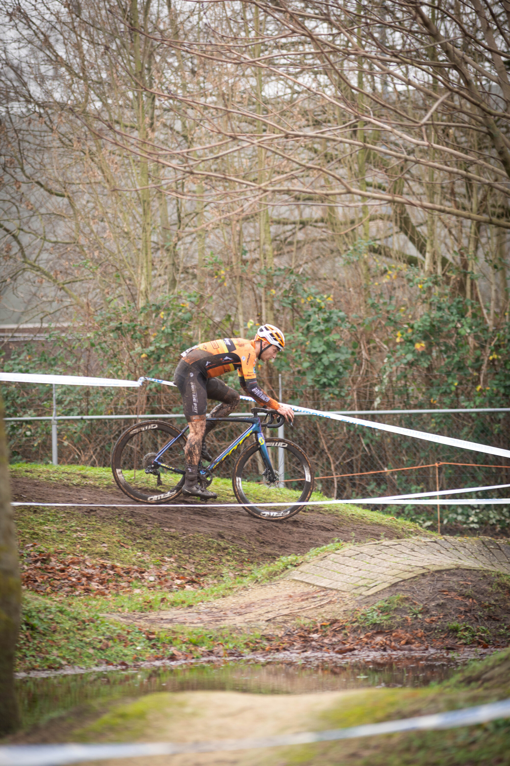 A man in an orange and black jersey riding a bicycle near water.