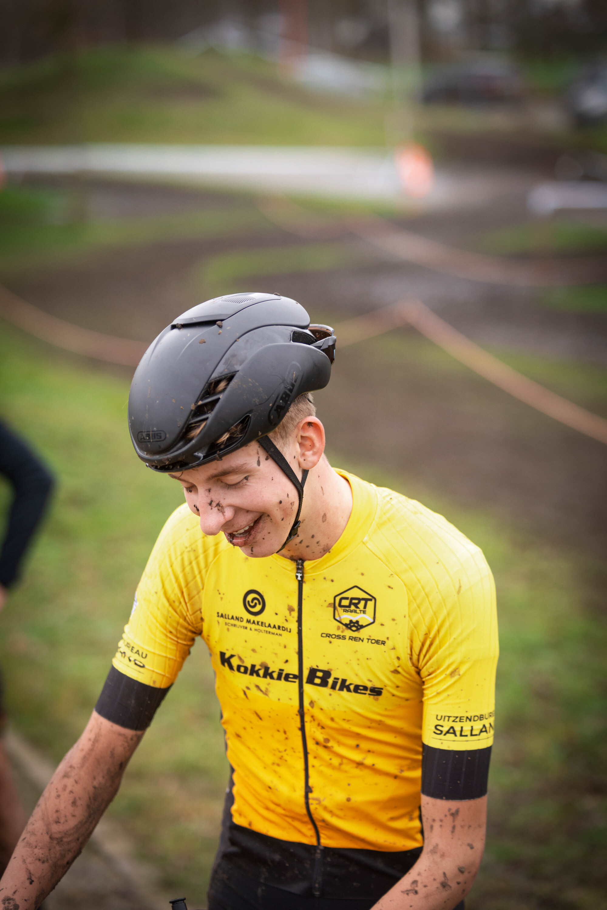 A man with a yellow GOW shirt and a black helmet is on a bicycle, smiling.