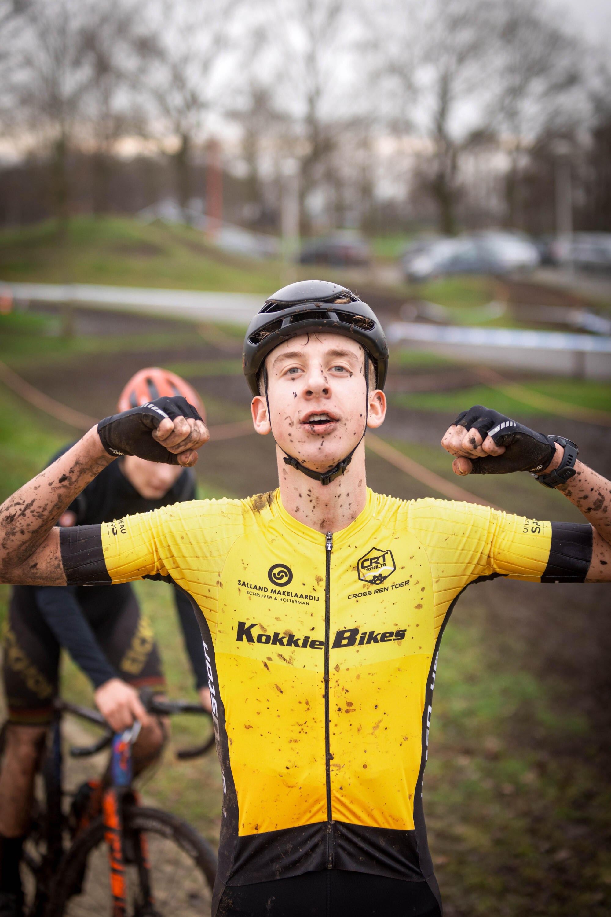 A young man wearing a helmet is in full sprint on his bike. His yellow and black outfit reads GO Raalte Cycling Team.