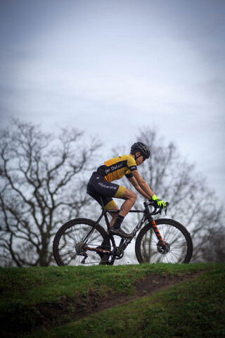 The man is wearing a yellow, black, and blue jersey while riding his bike.