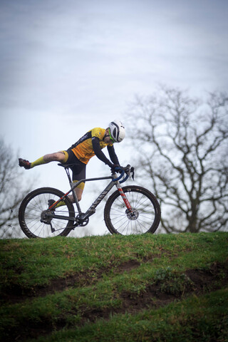 A man is riding a bike over a hill. The man is wearing a yellow and black jersey.