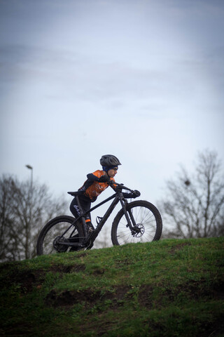 A person wearing a helmet is riding an orange and black bicycle.