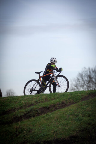 A person in a black helmet riding an orange and black bike on grassy terrain.