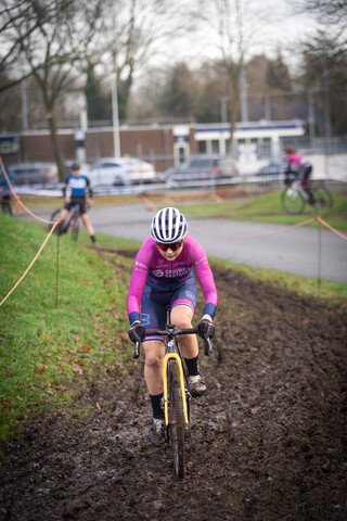 A cyclist in a pink jersey, numbered 7, races down the muddy track.