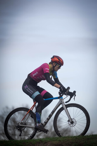 A woman riding a bicycle with blue and black colors on the bike. She is wearing a pink shirt and red helmet.