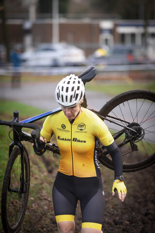 Woman holding a bicycle while wearing a yellow shirt with "Gow Raalte" on the chest.