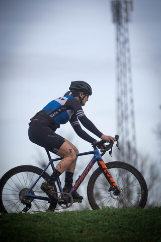 A cyclist in a blue and black uniform is riding his bicycle on a grassy field.