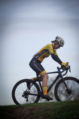 A woman in a yellow top and black cycling outfit is riding a black mountain bike.