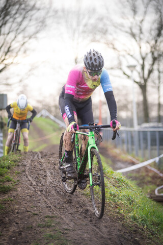 The cyclist is wearing a pink and blue shirt while riding on a dirt trail.