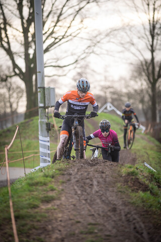 Three cyclists participating in a cyclocross competition sponsored by Ju/El/B/E/A/M.