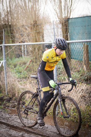 Cyclist riding a black bike in the rain wearing a yellow and black top.