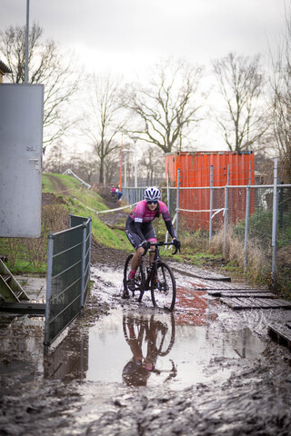 A person wearing a helmet riding a bicycle in the mud on a rainy day.