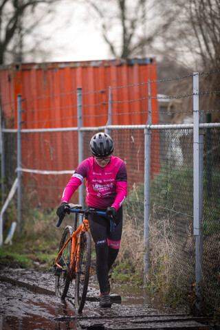 A person riding a bike in the rain, wearing pink and black.