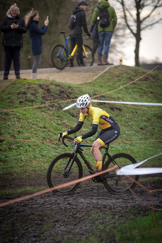 A man is riding a bicycle on a course with 9 other people standing and watching.