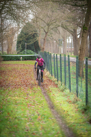 A woman in a purple shirt is riding a bicycle down a path.