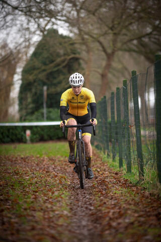 A cyclist in a yellow jersey rides along a trail surrounded by trees.