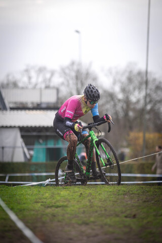 A woman is riding a green bicycle and wearing a pink top, black pants and a helmet.