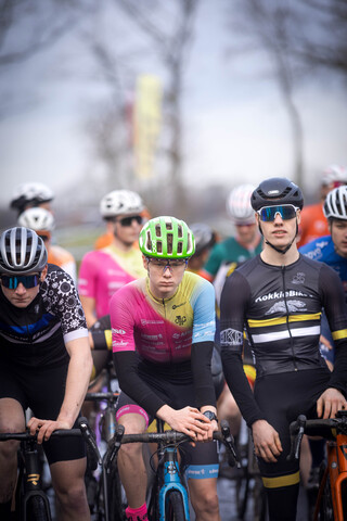 Group of cyclists in a race, one wearing a blue and black shirt with "Gow Raalte" on it.