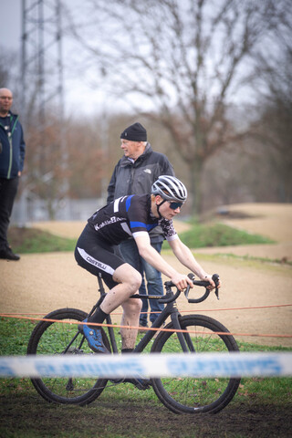 A man wearing a black and white shirt is riding his bicycle in a competition, sponsored by GOW Raalte.