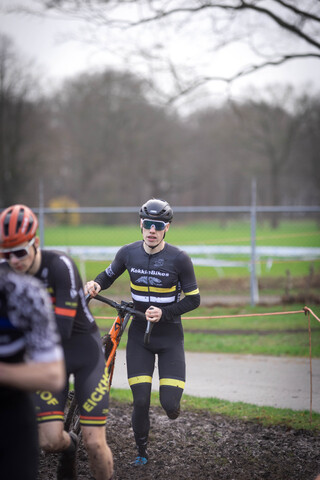 A person in black and yellow jumps a bicycle on the track.