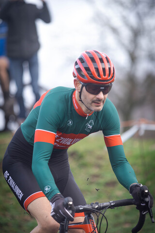 A cyclist on a track wearing a green and red jersey with the word cyclocross on it.