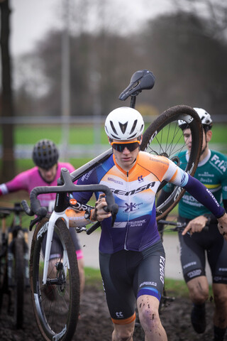 A cyclist is holding a bike and wearing a GOW Raalte cycling outfit.