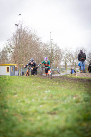 Two cyclists wearing safety helmets are riding on a dirt course at the 2023 Cyclocross event.