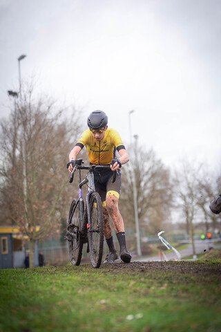 A man in a yellow shirt and black helmet riding his bike down a muddy path.