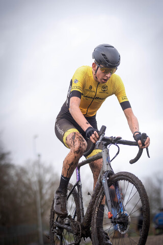 A man wearing a yellow and black jersey is riding a bike in the rain.