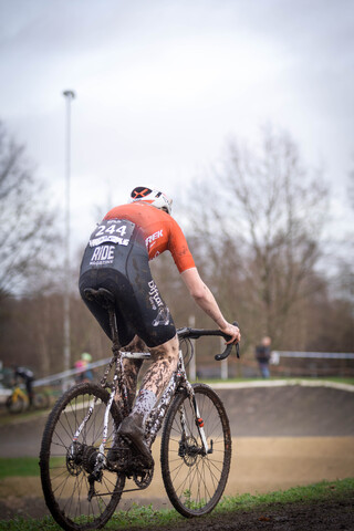 A man wearing the number 20243 is riding a bicycle with tire tracks in the background.