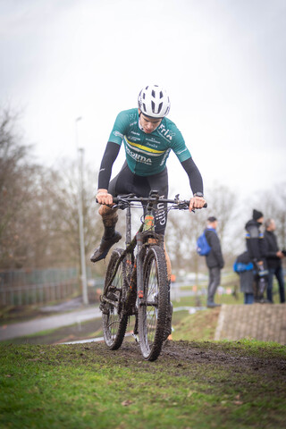 A cyclist in a green jersey, bearing the number 17 on his back and the letters "Ju/El/Ba/Am" is in motion.