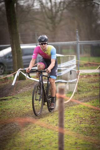 A man in a pink shirt rides a bicycle past a white fence.