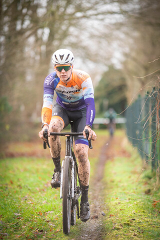 A cyclist riding through a wooded area with a black and orange shirt on.