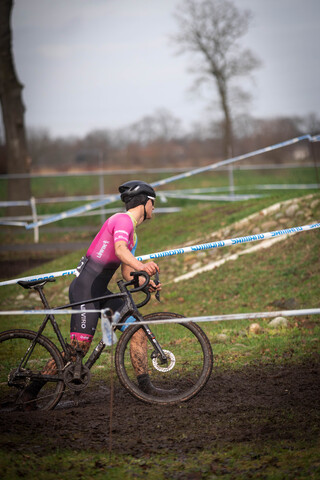 A cyclist wearing a pink shirt is riding through the mud on his bike.