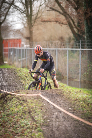 A biker in a black and red outfit is riding his bike down a dirt path.